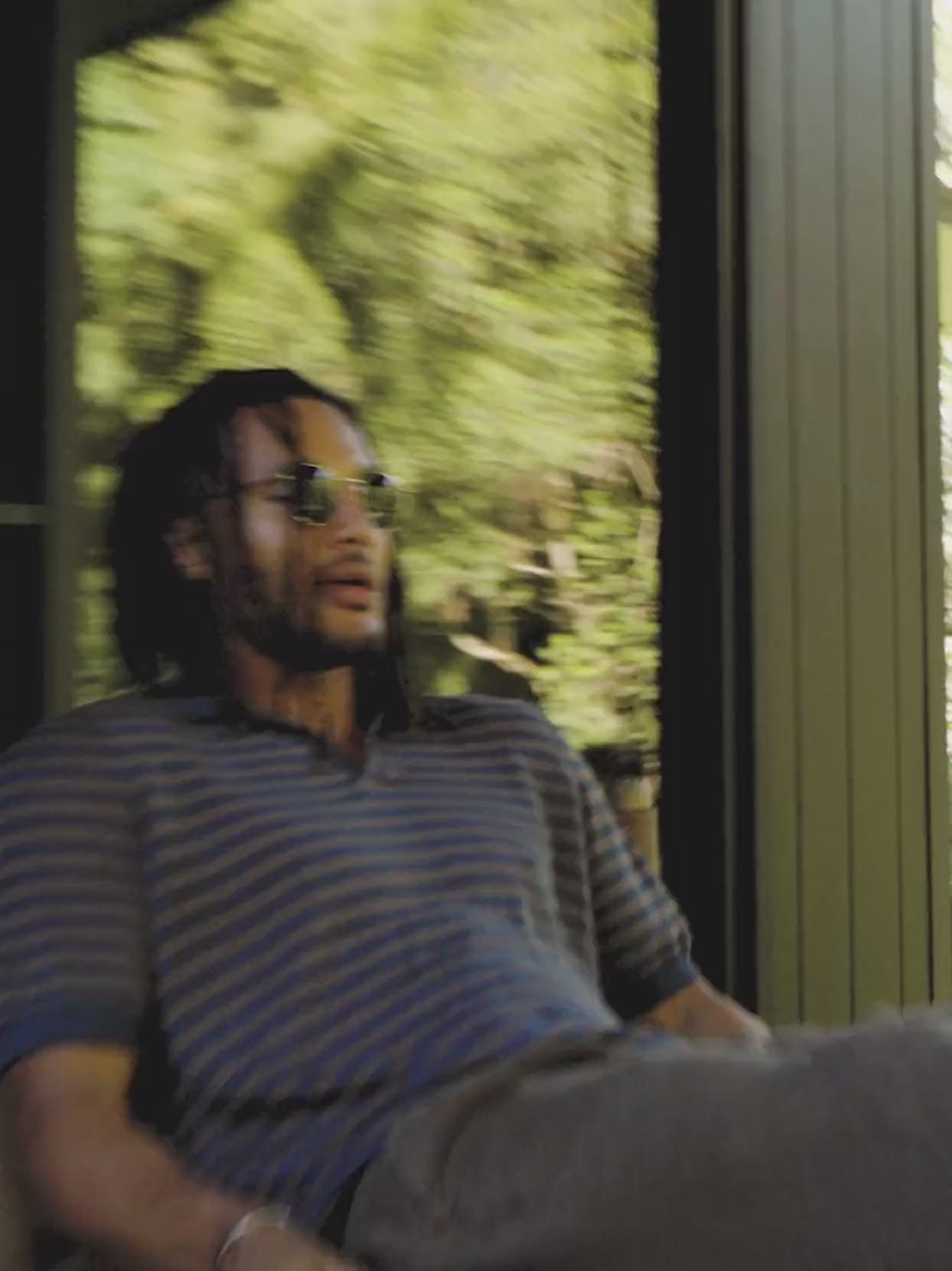 Video of a man wearing a striped short sleeve shirt and pants sitting in a chair