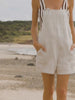 Video of a woman wearing a flax romper over a brown striped swimsuit walking along the beach